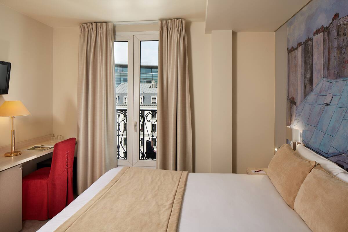 Une chambre d’hôtel avec un lit, un bureau et une chaise, une télévision et un tableau au mur.