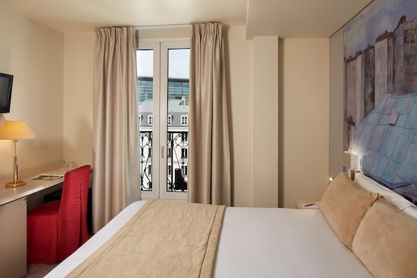Habitación de hotel con cama, escritorio con silla, televisor y un cuadro en la pared.