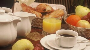 A breakfast table with croissants, a fruit basket, a pitcher, a glass of orange juice, and a cup of coffee. - Golden Tulip Washington Opéra (Paris)