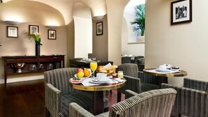 A dining area with striped upholstered chairs, round tables, and a buffet table with breakfast items. - Golden Tulip Washington Opéra (Paris)