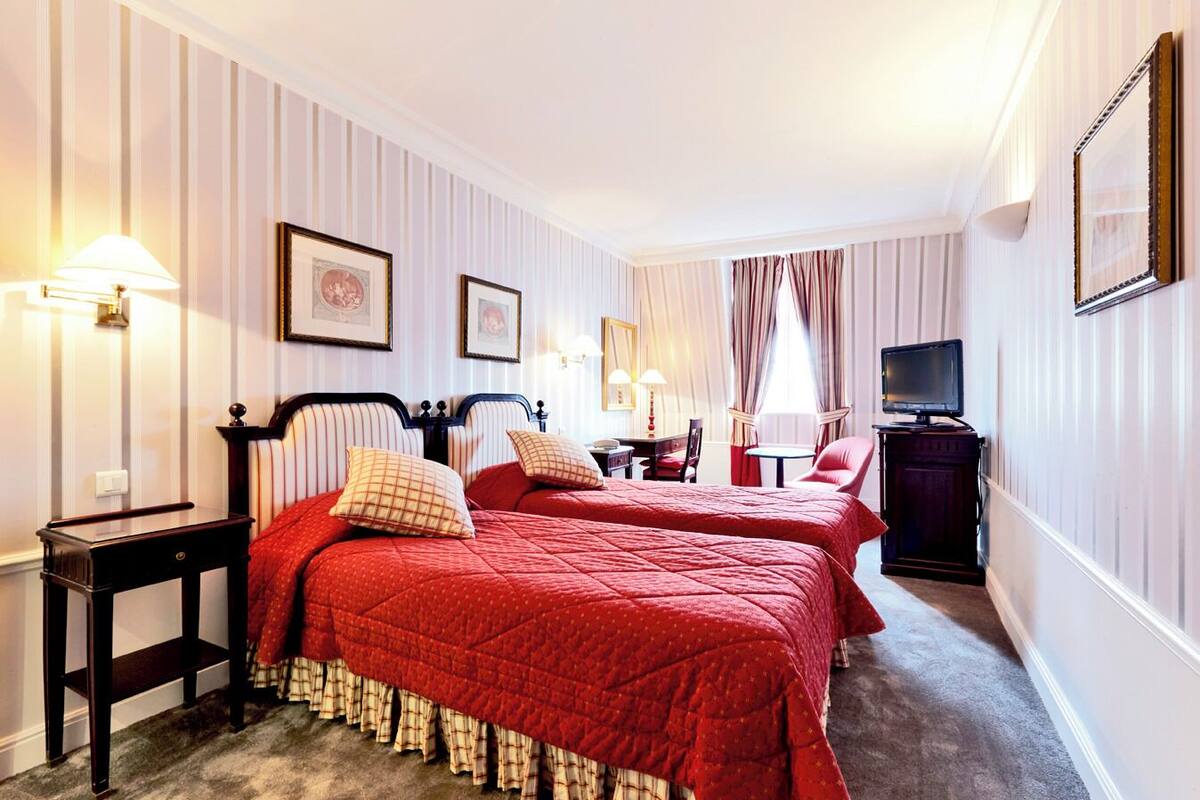 A hotel room with two beds, a TV, a desk, and a chair.
