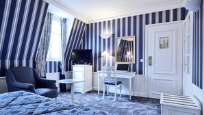 A hotel room with a bed, a desk, a chair, a television, and a window with curtains. - Golden Tulip Washington Opéra (Paris)