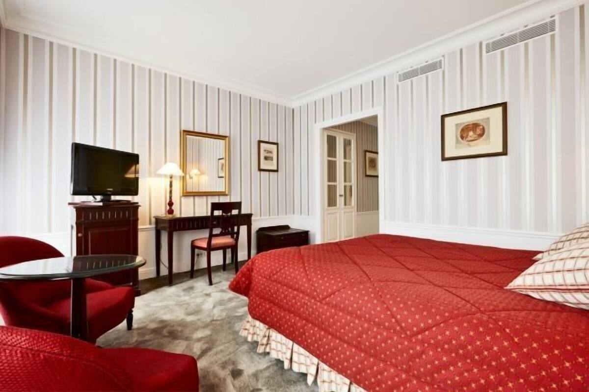 A hotel room with a bed, a desk, a chair, a television, and a mirror.