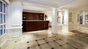 A spacious lobby with a marble floor, a central wooden reception desk, and a bookshelf filled with books. - Golden Tulip Washington Opéra (Paris)
