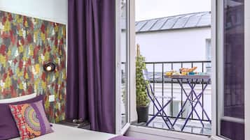 A bedroom with a large window, a balcony with a table and chairs, and a colorful floral wallpaper.