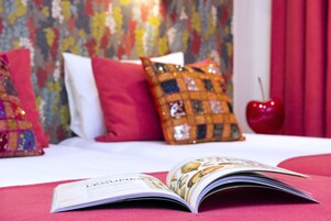 Een bed met een tijdschrift, kussens en een rode appel op een tafel.