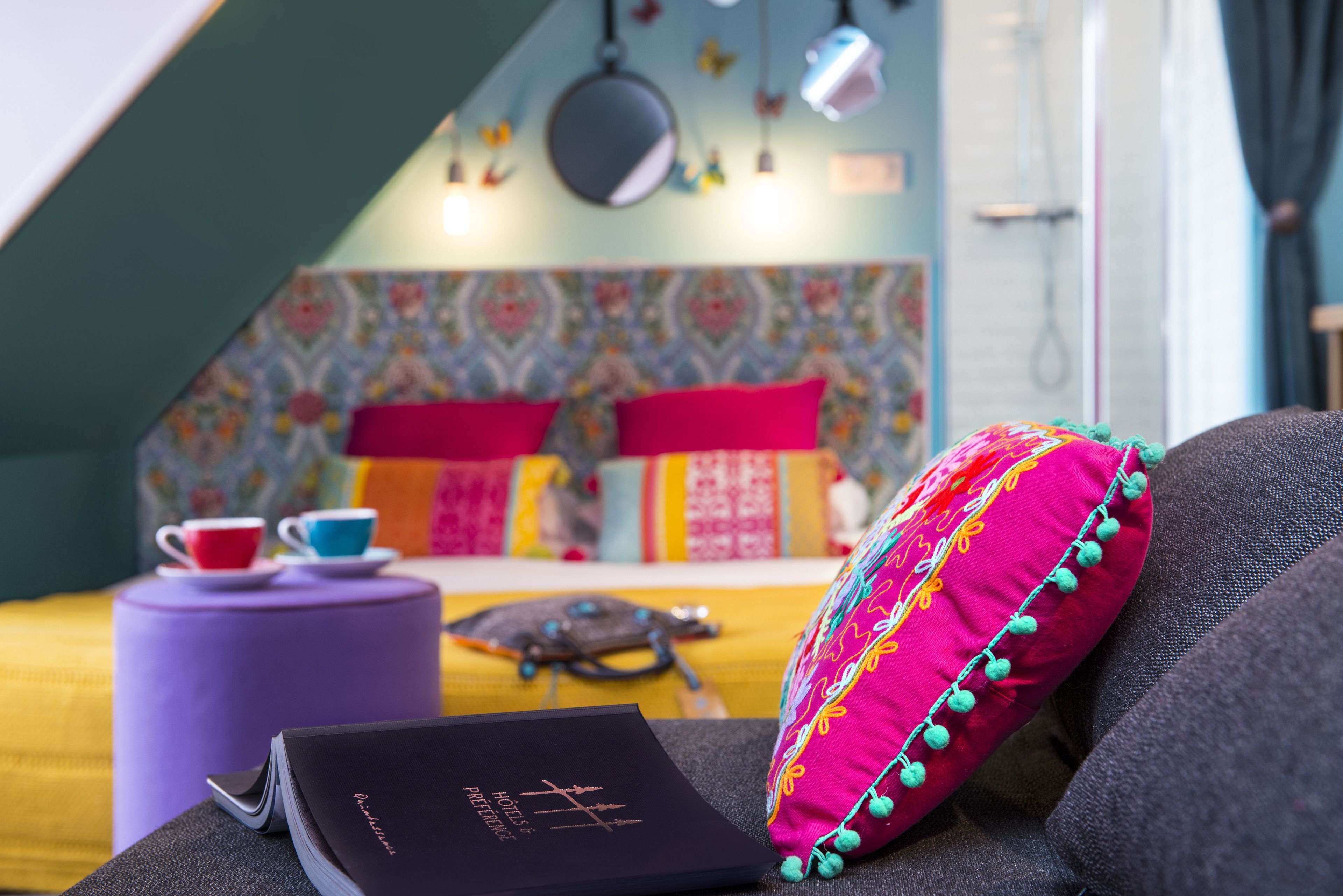 A cozy room with a bed, a purple ottoman, and a book titled "Hotel de Paris."