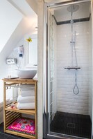 A modern bathroom with a glass-enclosed shower, a white tiled wall, and a wooden vanity with a large bowl sink.