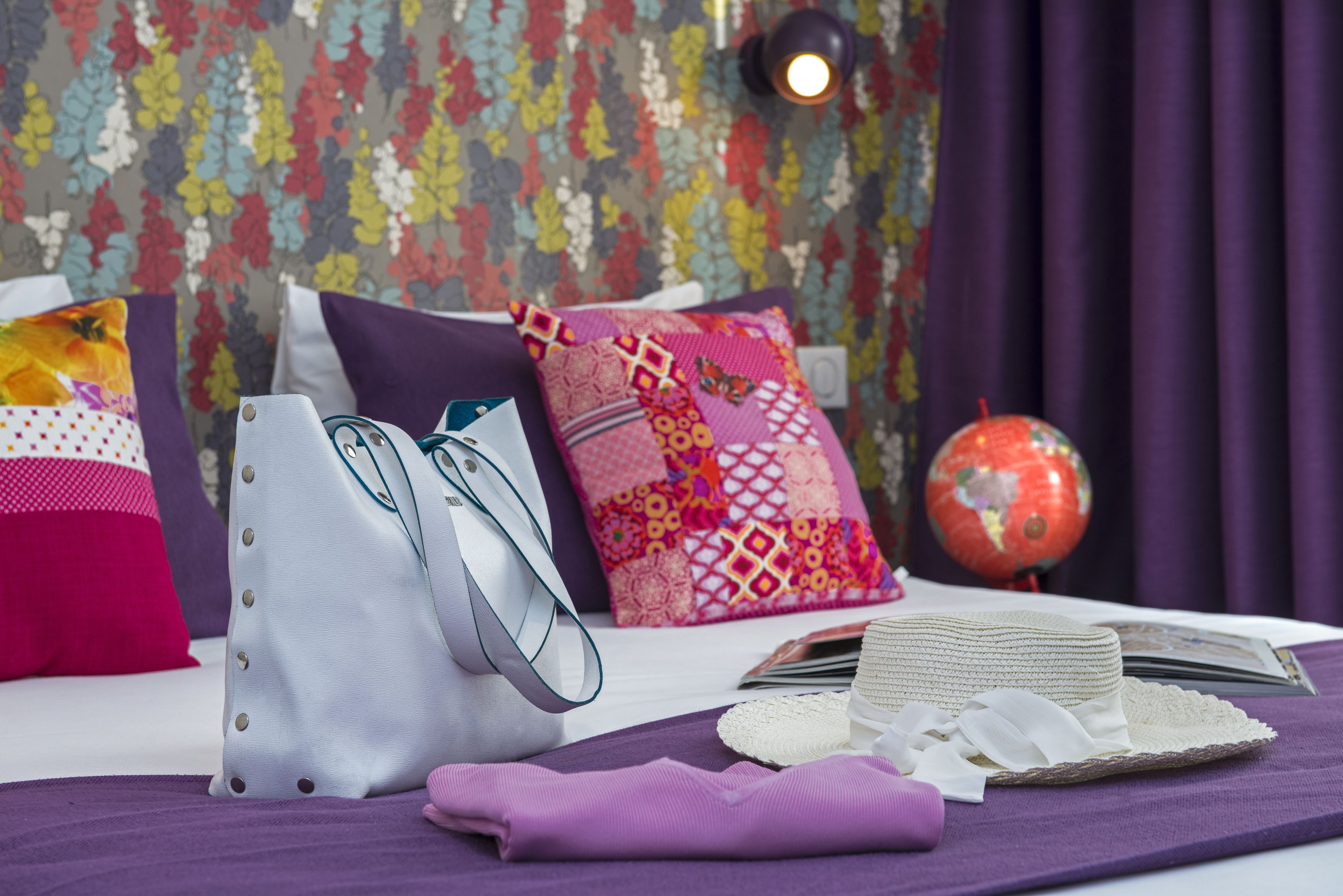 Una cama bien ordenada con almohadas coloridas, un globo terráqueo y una pila de libros.
