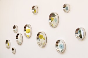 Una serie de espejos ovalados con superficies reflectantes y diseños decorativos, colocados sobre una pared lisa.