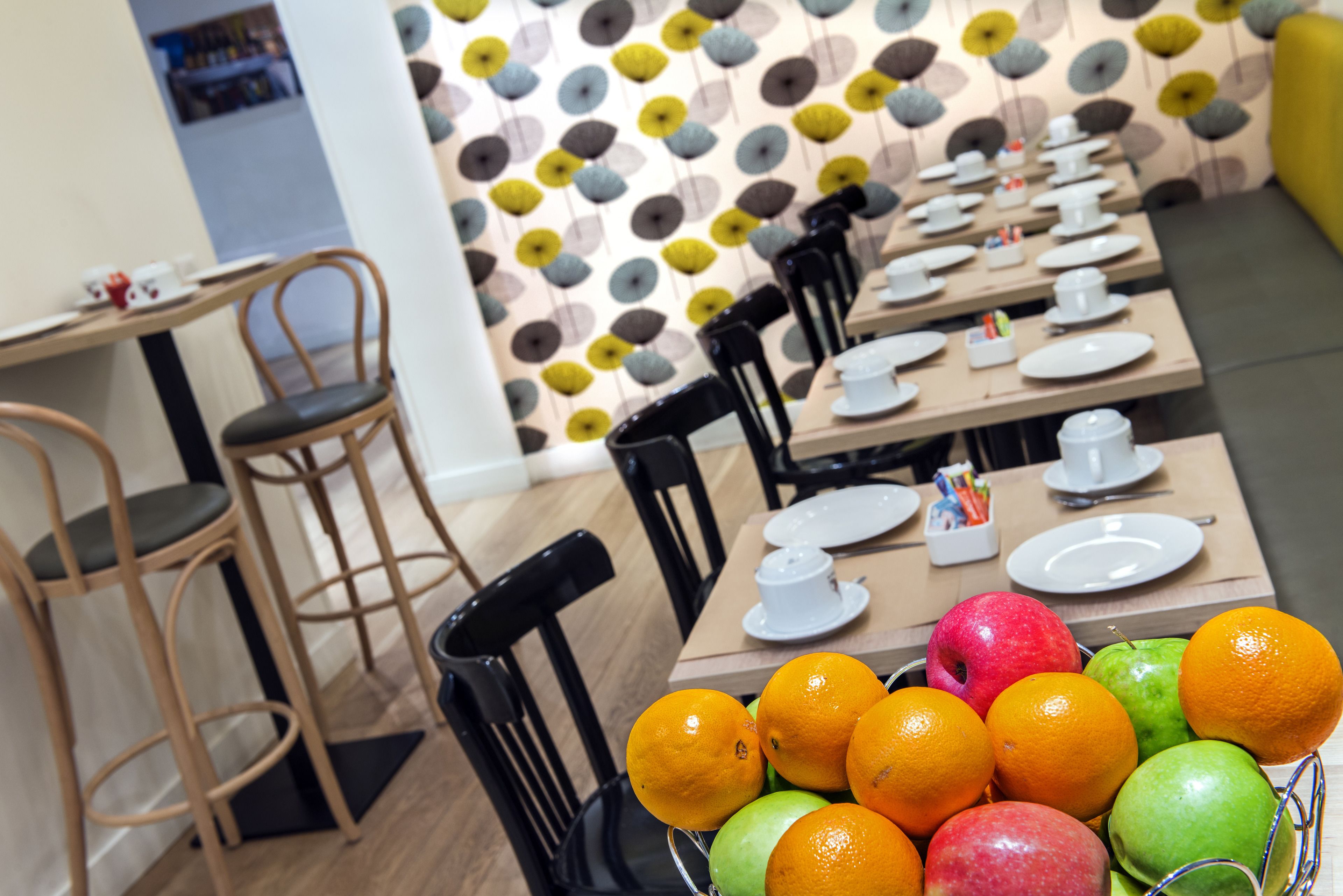 A dining area with tables set for service, chairs, and a fruit basket with oranges and apples.