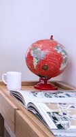 A globe on a wooden stand with a white mug beside it, and an open magazine on a wooden surface.
