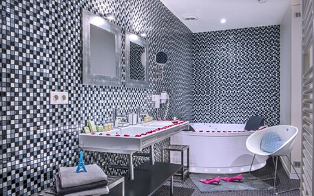 A modern bathroom with a checkered tile backsplash, a large mirror, a white bathtub, a white chair, and a vanity with a sink and towel rack.
