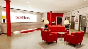 A hotel lobby with red sofas, a reception desk, and a large 'DORMERO' sign.