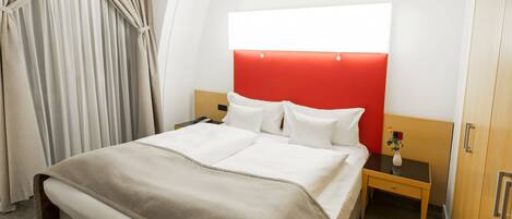 Habitación de hotel con una cama grande, una mesita de noche y una pared de acento roja.
