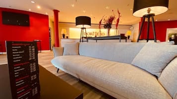 A modern hotel lobby with a white sofa, a reception desk, and a menu board.