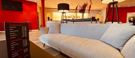 A modern hotel lobby with a white sofa, a reception desk, and a menu board.