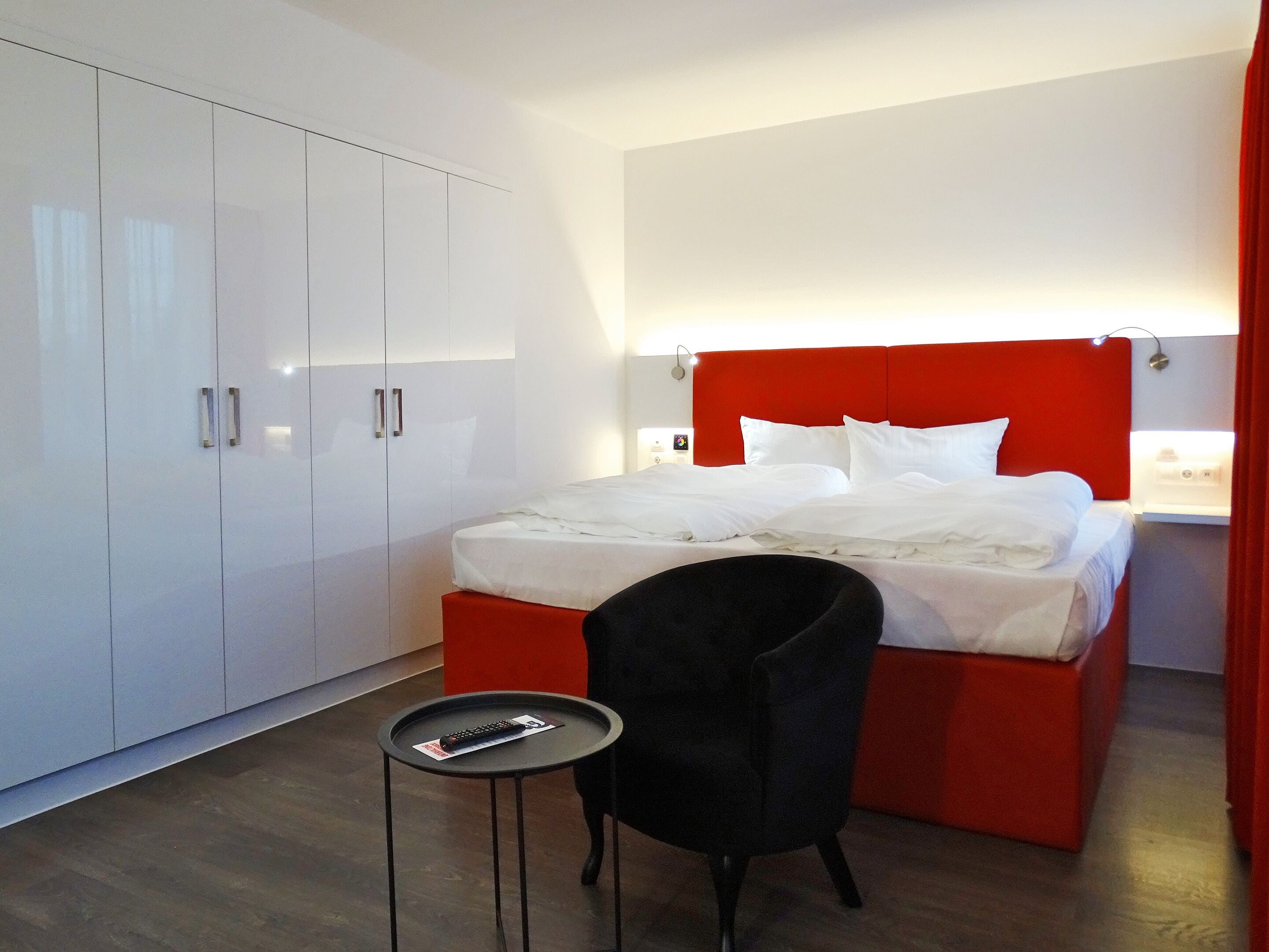 A hotel room with a bed, a small table, a chair, and a wardrobe.