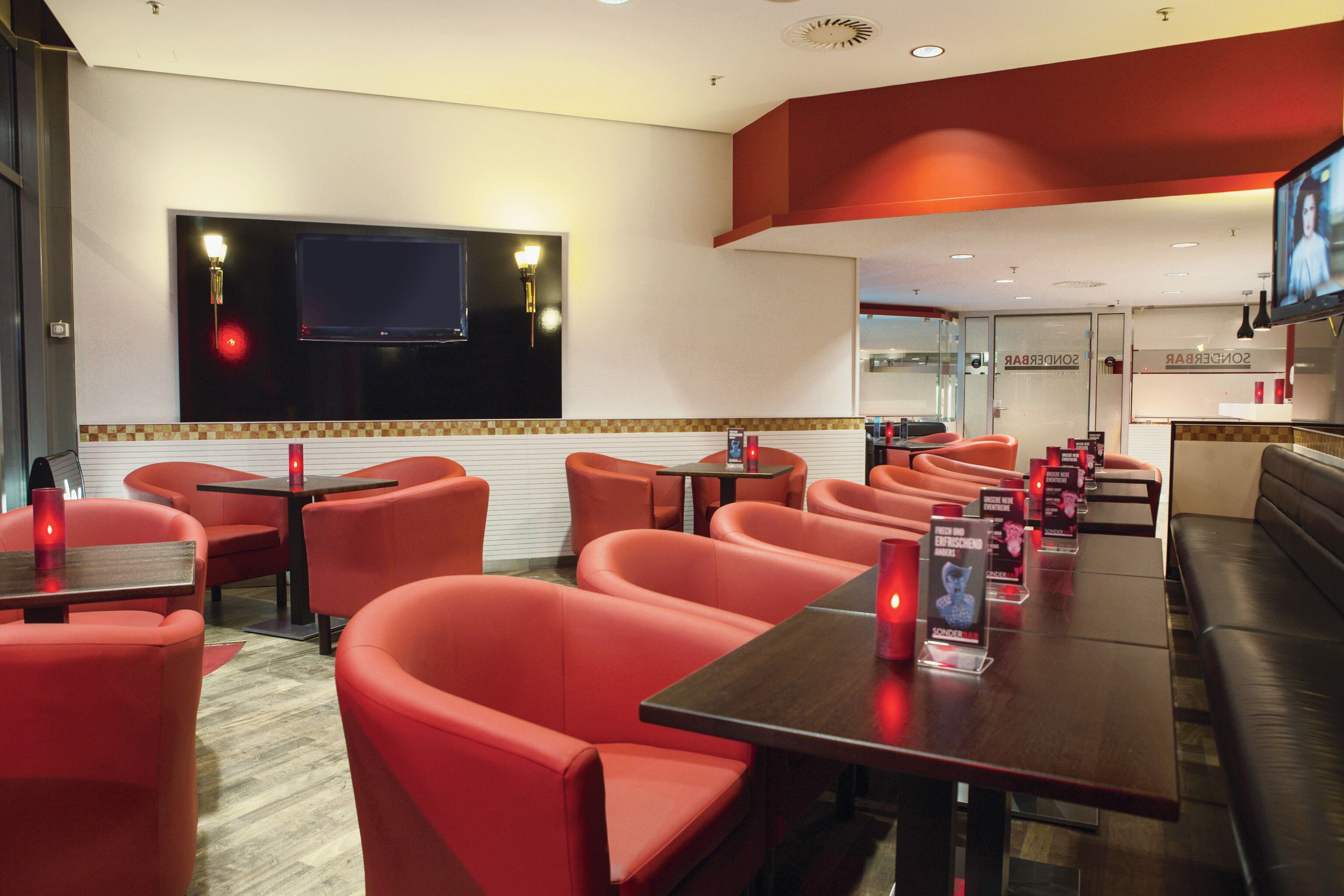A restaurant with red seating, a TV mounted on the wall, and a counter with a menu.