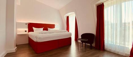 Una habitación de hotel moderna con una cama roja, una mesita y una silla.