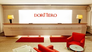 Een moderne hotellobby met een receptiebalie, een rode fauteuil en een kleine ronde tafel.