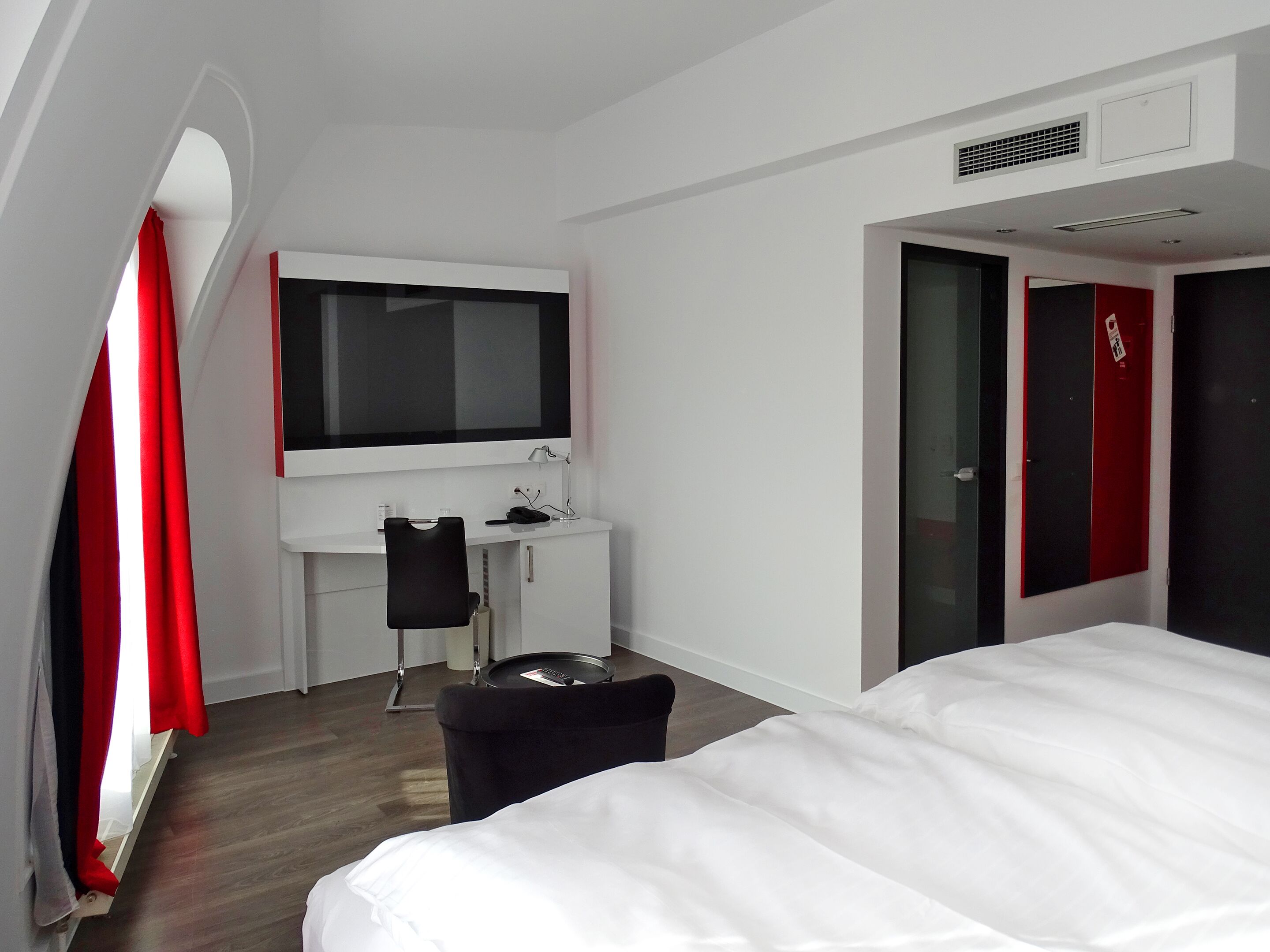 A hotel room with a bed, a desk with a chair, a TV, and a wardrobe.
