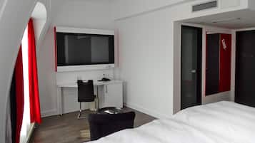 A hotel room with a bed, a desk with a chair, a TV, and a wardrobe.
