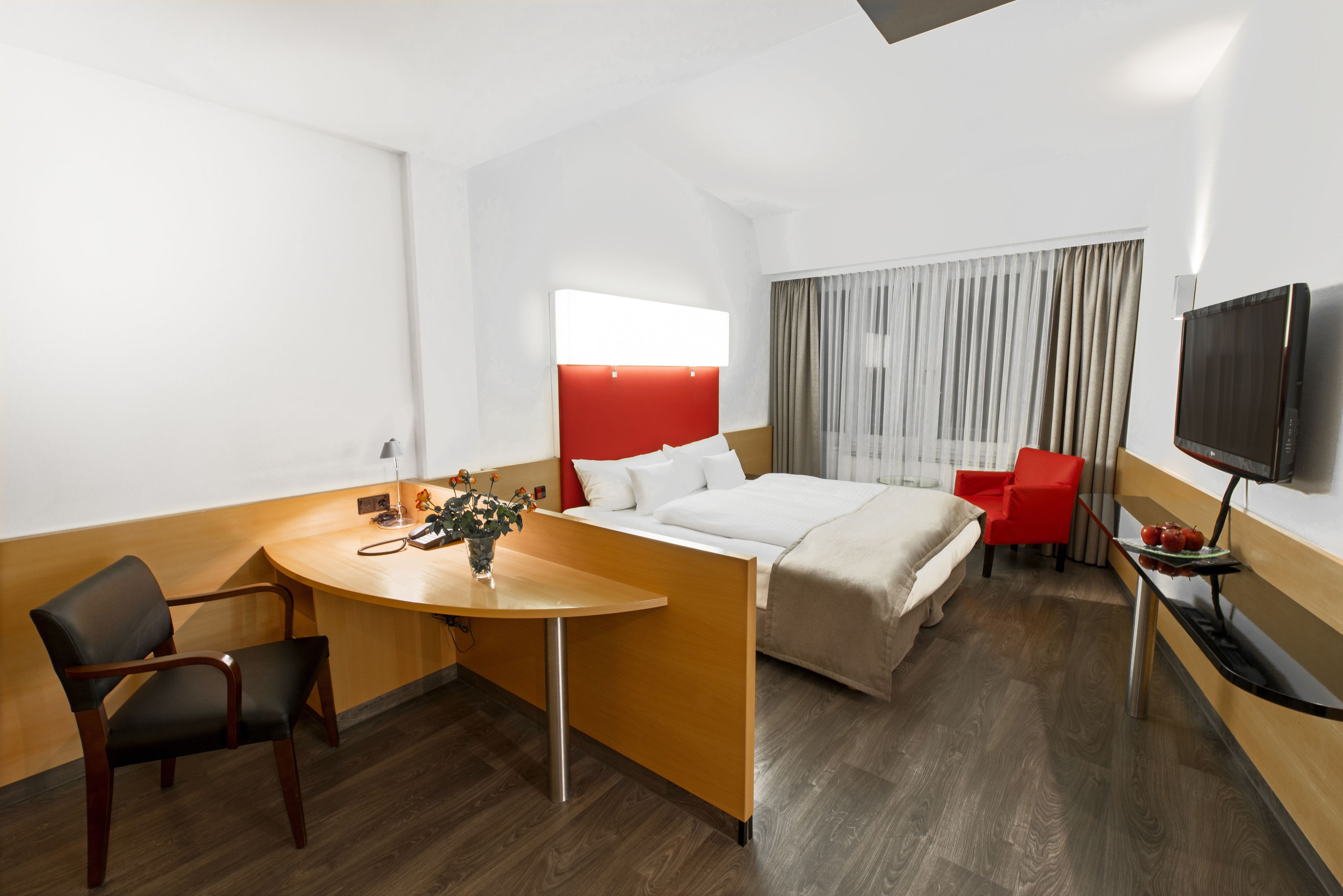 A hotel room with a bed, a desk, a chair, a TV, and a window with curtains.