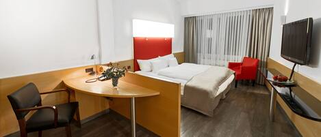 Habitación de hotel con cama, escritorio, silla, televisor y ventana con cortinas.