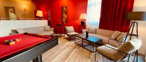 A hotel room with a pool table, a sofa, a coffee table, and a red accent wall.