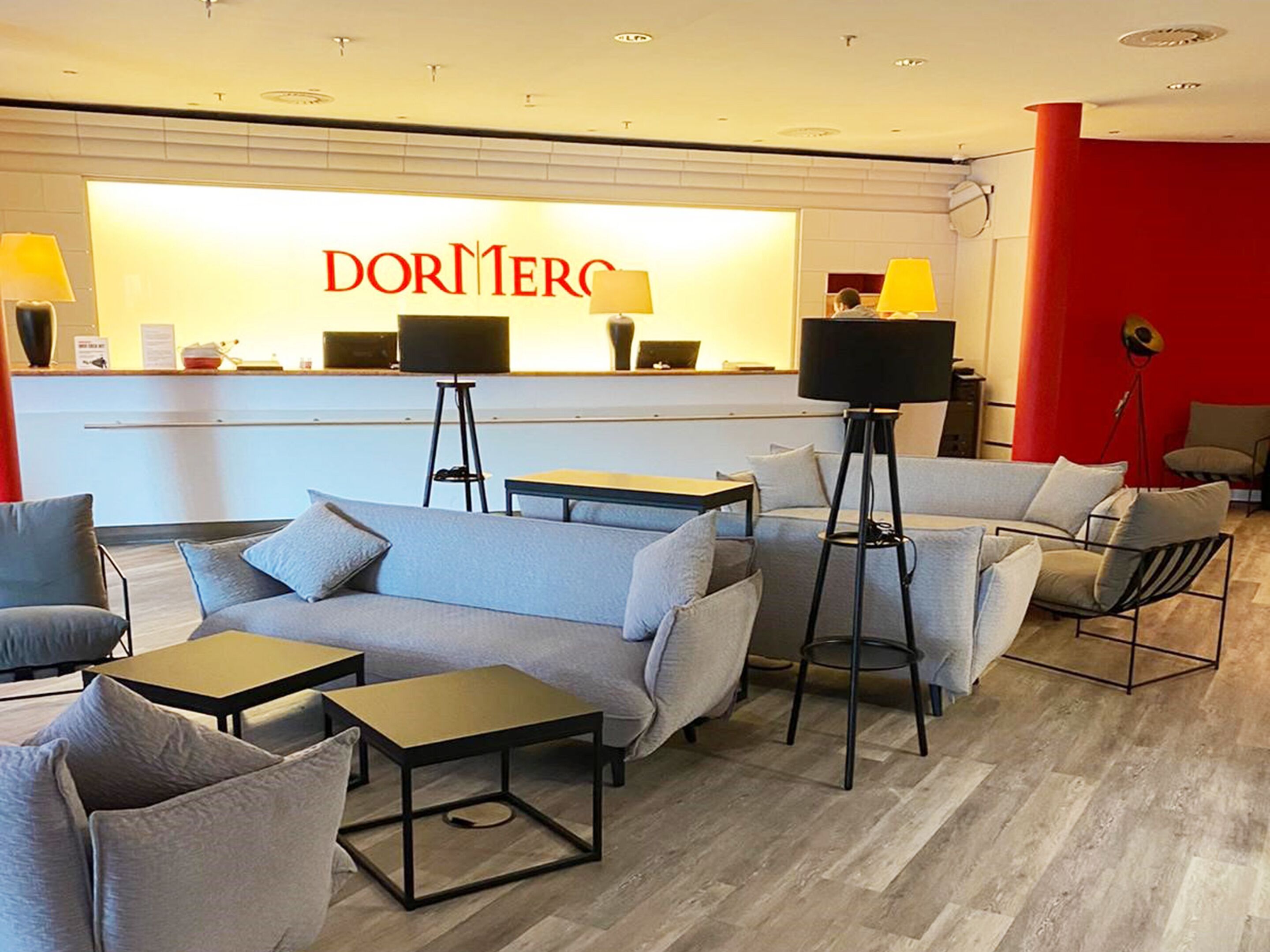 A modern hotel lobby with a reception desk, sofas, and tables.