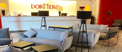 A modern hotel lobby with a reception desk, sofas, and tables.