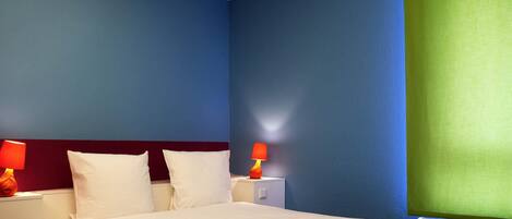 A hotel room with a bed, two bedside tables with lamps, and a window with a green blind.