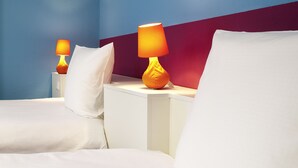 Habitación de hotel con dos camas, ropa de cama blanca y dos lámparas de noche con pantallas naranjas.