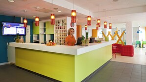 A reception area with a counter, a digital screen, and a clock on the wall. - ibis Styles Düsseldorf - Neuss (Neuss)