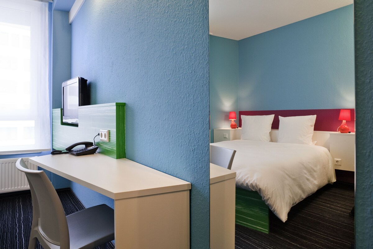 A hotel room with a desk, chair, and bed.