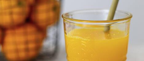 Un vaso de jugo de naranja con una pajita, y un fondo desenfocado de naranjas.