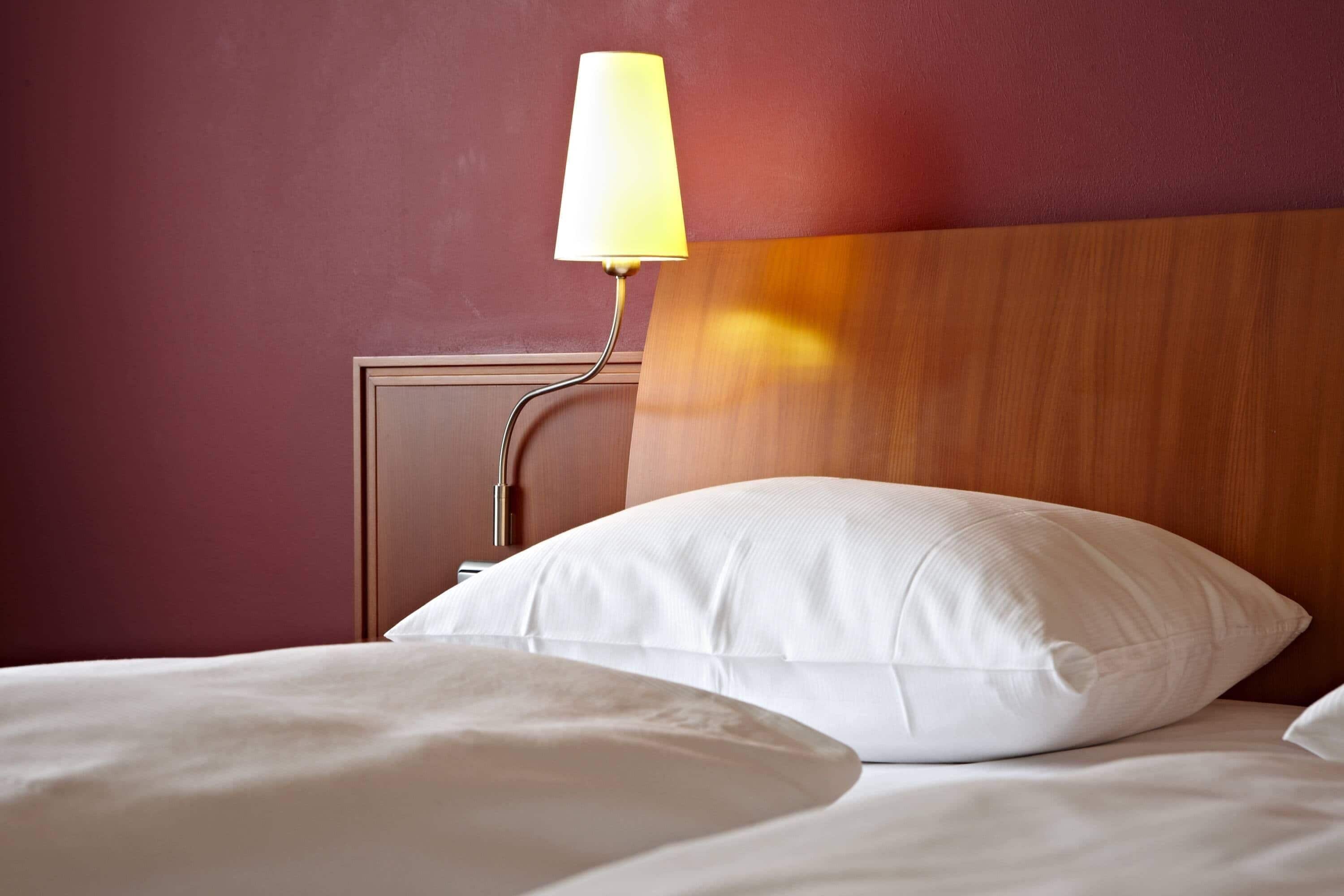 A hotel room with a bed, a nightstand with a lamp, and a wooden headboard.