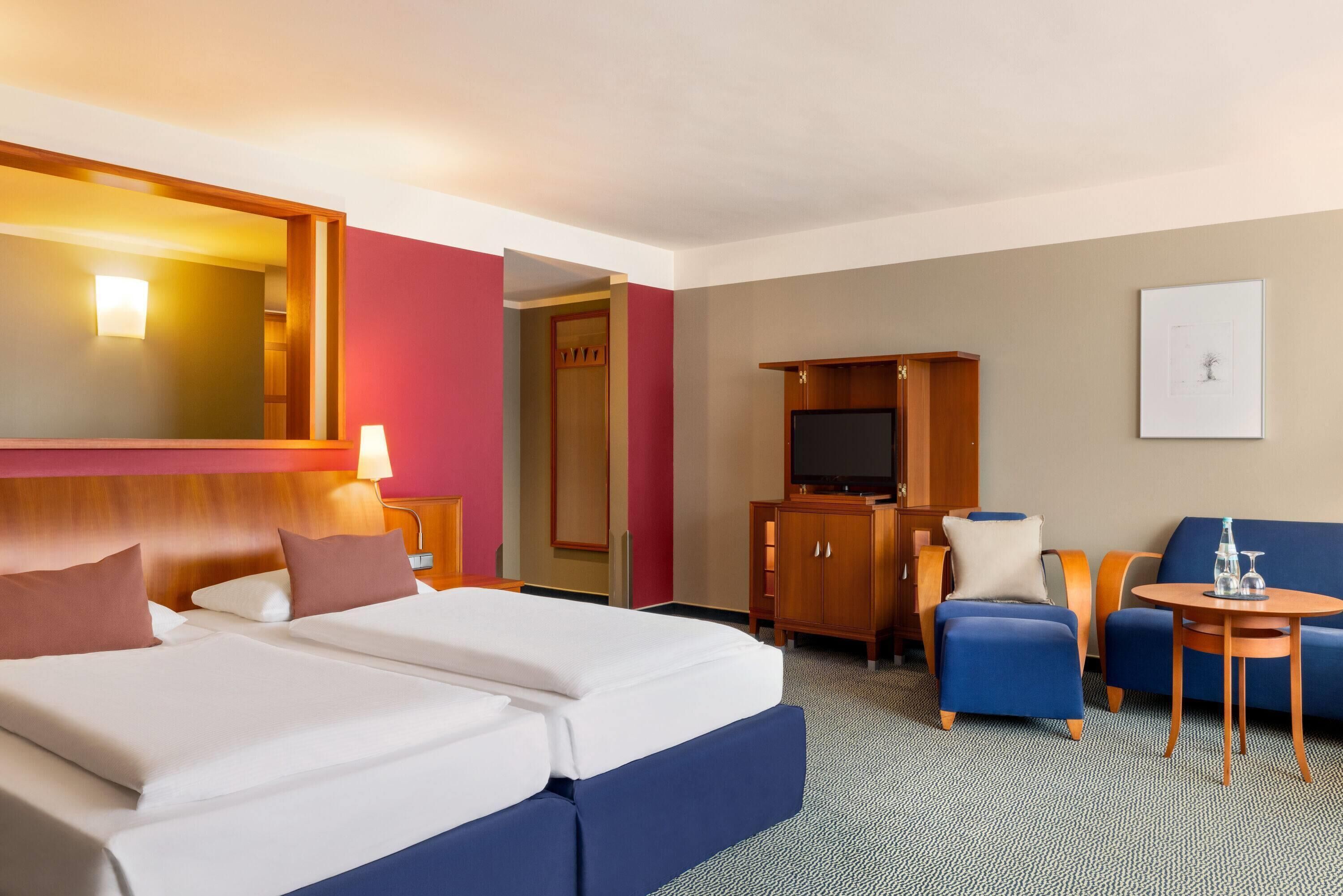 Habitación de hotel con cama, televisor, escritorio, silla, sofá y una mesita.