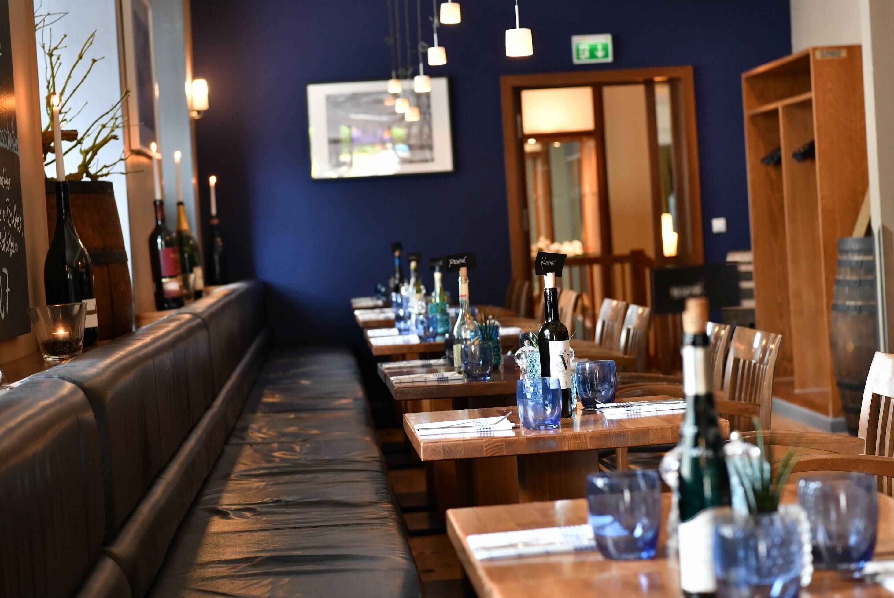 A restaurant interior with wooden tables, cushioned benches, and hanging pendant lights.