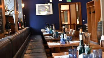 A restaurant interior with wooden tables, cushioned benches, and hanging pendant lights.