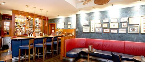 A bar area with stools, a bar counter, and a red cushioned seating area.