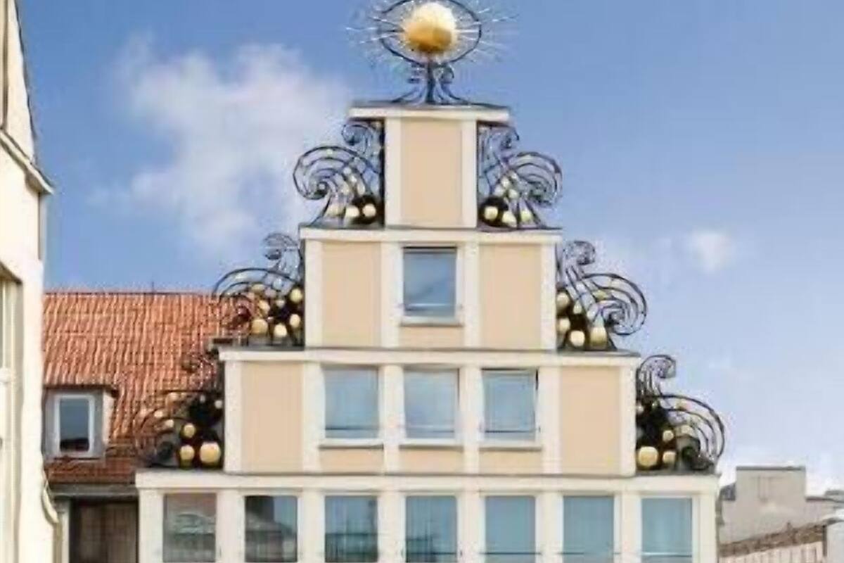 A multi-story building with a symmetrical facade, large windows, and decorative ironwork on the roof.