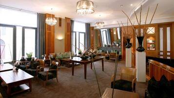 Eine geräumige Hotelhalle mit einem Holzbüro, gemütlichen Sitzbereichen, großen Fenstern und dekorativen Vasen.