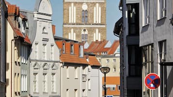 A street view with a historic tower, a building with a clock, and a no parking sign.