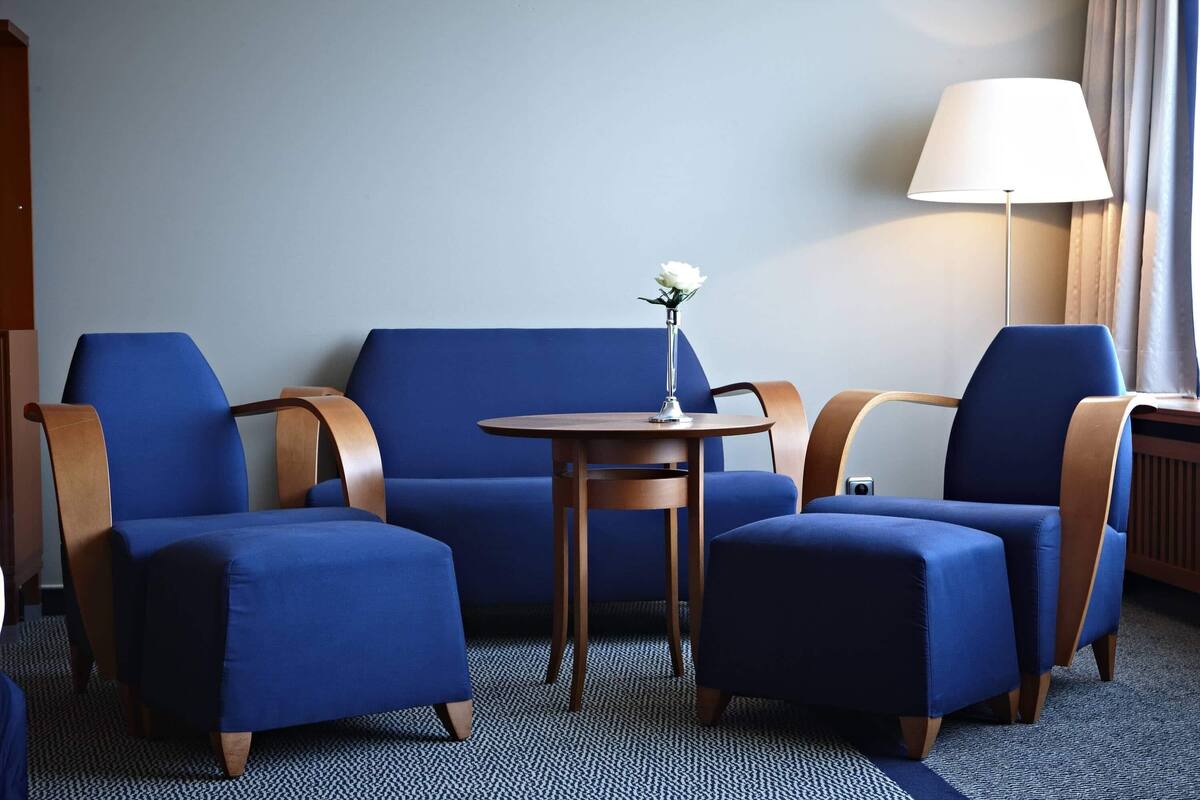 A room with a blue sofa, two armchairs, a small round table with a flower, and a lamp.