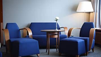 Een kamer met een blauwe bank, twee fauteuils, een kleine ronde tafel met een bloem en een lamp.