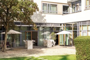 Un edificio moderno con un espacio de estar al aire libre techado, puertas de vidrio y un árbol.