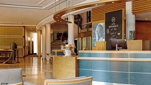 A hotel lobby with a reception desk, seating area, and a staircase.