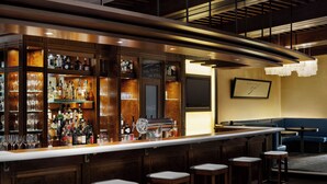 A bar area with a long counter, multiple stools, and a variety of bottles and glasses.
